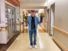 Image of Bobby Patton holding bouquets of flowers in a hospital corridor. 