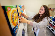 Person arranges boxed cereal products on a store shelf in a controlled retail lab setting, examining packaging and product placement.