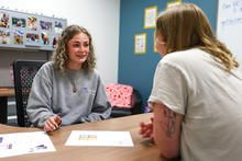 Person seated at a table speaking with another person during a one-on-one meeting in an office.