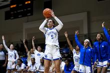 blair green in a kentucky basketball uniform shooting a three. her teammates are standing behind her cheering her on.