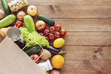 Paper grocery bag with fresh vegetables, fruits, milk and canned goods on wooden backdrop