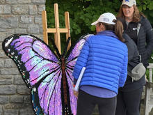 A large purple-and-blue Lego butterfly display stands outdoors as two women pause to admire it.