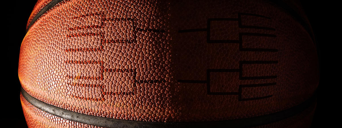 A close‑up photograph of a basketball set against a dark background. The ball is lit from the left side, revealing its textured surface.