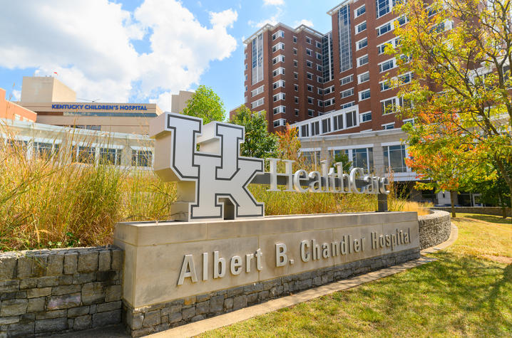 Exterior view of UK HealthCare’s Albert B. Chandler Hospital with its sign in the foreground and surrounding buildings under a bright sky.