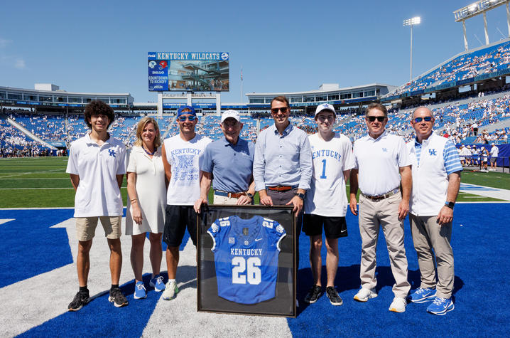 Photo of people standing on football field behind a framed jersey.