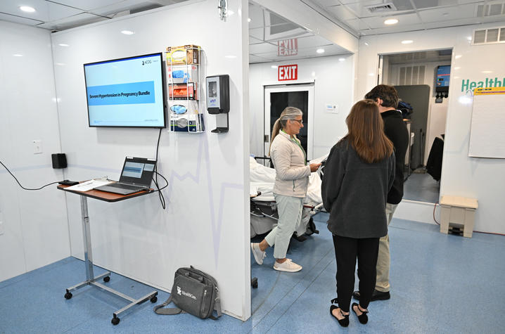A doctor stands in a mobile clinic near an OB simulator with two other people in the room