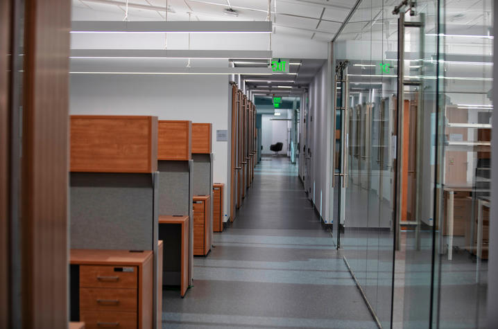 A dimly lit hallway with cubicles to one side and glass walled offices to the other.