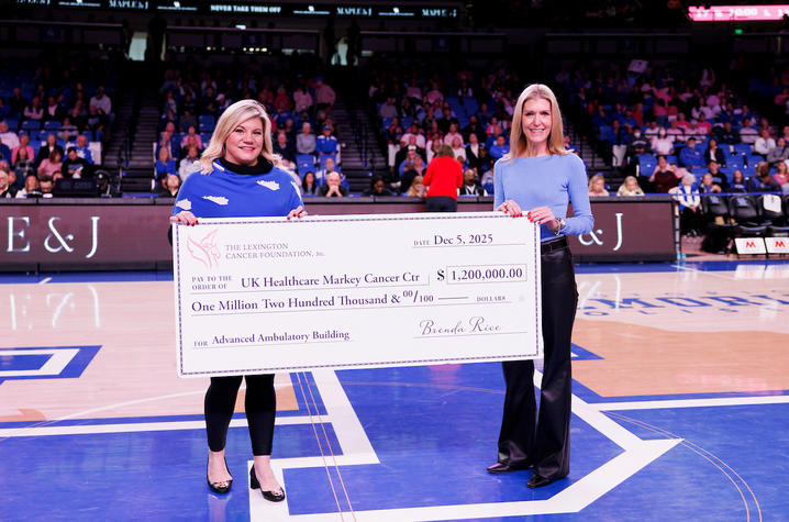 Photo of Lisa Mahan and Kristi Martin with large check Two individuals standing at center court of a basketball arena holding an oversized ceremonial check for $1,200,000 from The Lexington Cancer Foundation to UK Healthcare Markey Cancer Center for an Advanced Ambulatory Building