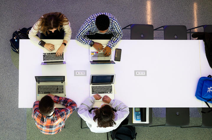 students on laptops sitting around a white table shot from above