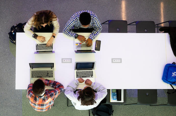 Overhead view of five people working on laptops around a long table.