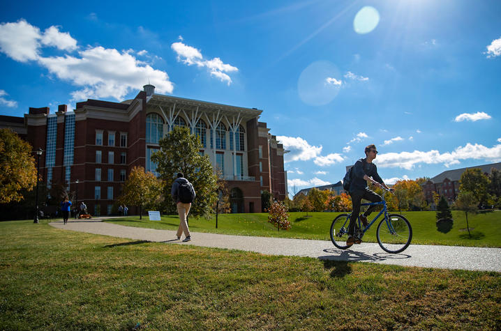 photo of student walking passing student on bike around the bowl of Young Library