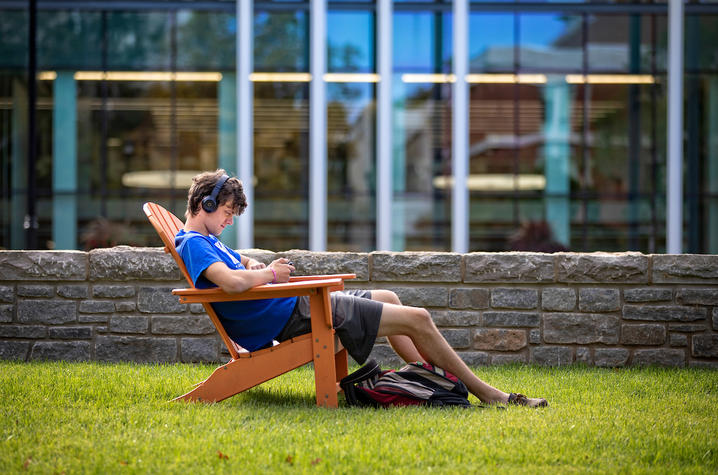 male student with headphones on sitting in an outdoor chair