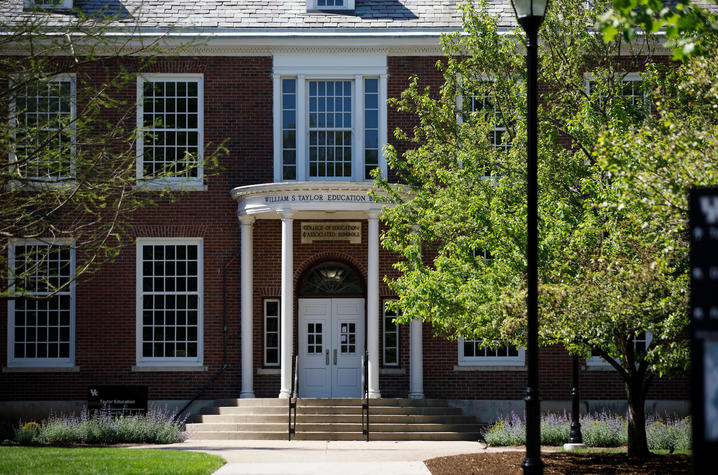 This is a front-view photo of the UK Taylor Education Building with trees and grass in sunlight in the foreground.