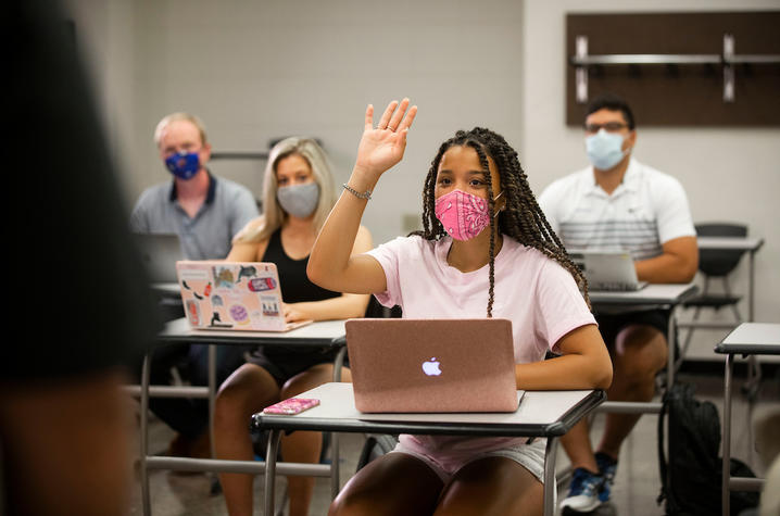 photo of students in class and one raising her hand to ask a question