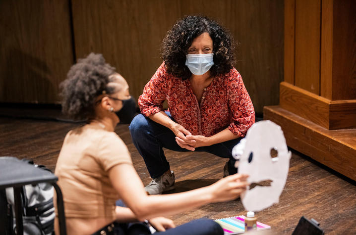 photo of Nancy Jones looking at students Greek mask in theatre class