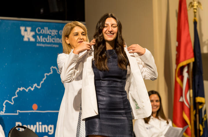 A woman in a white coat helps a young woman put on a white coat.