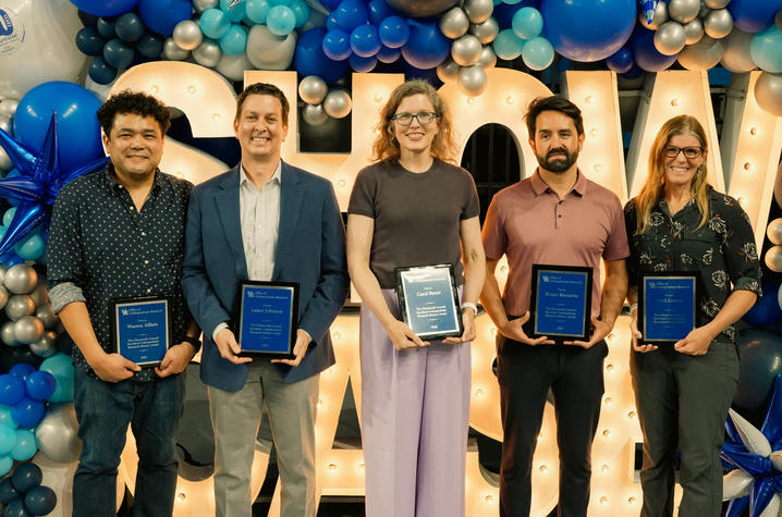 photo of faculty mentor award winners Five individuals stand side by side holding framed awards in front of a balloon arch backdrop.