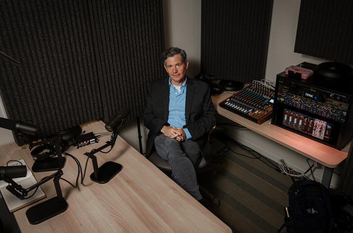 Wide view of a recording studio with microphones, audio mixers and production equipment. A person sits between recording stations, highlighting the professional environment used for audio storytelling and oral history interviews.
