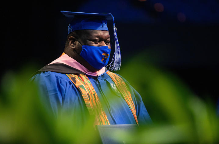 photo of masked Reginald Smith Jr. in cap and gown holding diploma at Commencement
