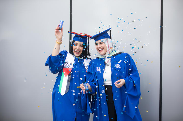 Two UK graduates in caps and gowns with confetti
