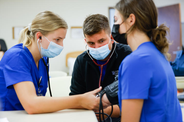 image of nursing student Colin Goodfellow watching other nursing students take blood pressure readings