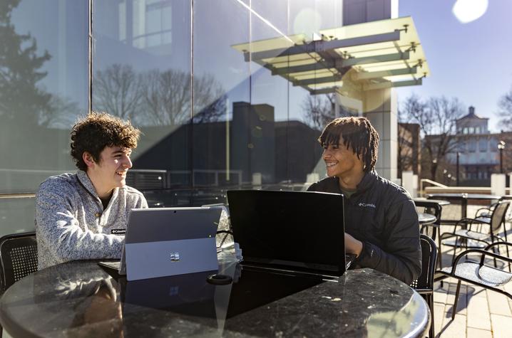This is a photo taken outside on UK's campus of two students working and talking.
