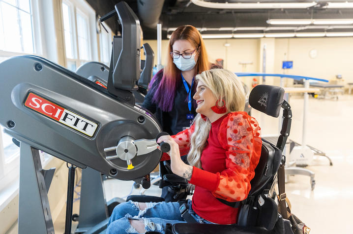 kayla lacy working with a hand bike in the rehabilitation gym alongside her occupational therapist.
