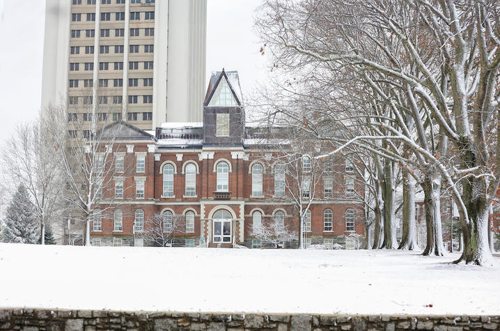 Snow-covered campus scene featuring a historic brick building and tall tower.