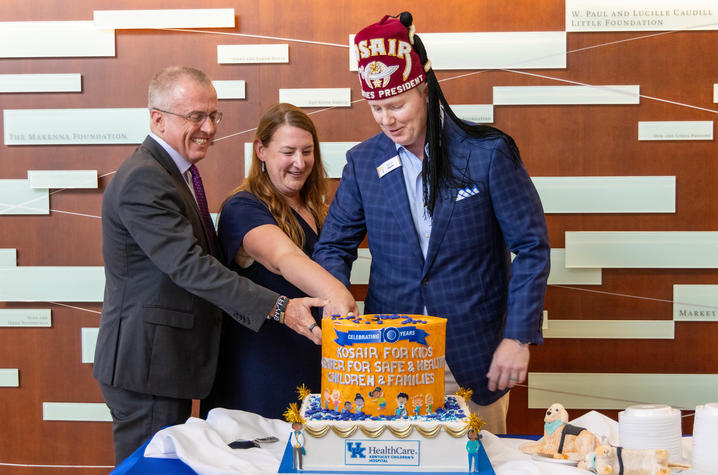 Photo of Scottie Day, Christina Howard and Barry Dunn Three people are cutting a decorated cake on a table. The cake reads “Kosair for Kids – Hope for Safe & Healthy Children & Families” and features blue and yellow colors.