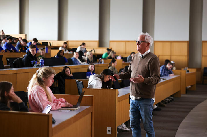 An instructor speaks to students seated in a large lecture hall.