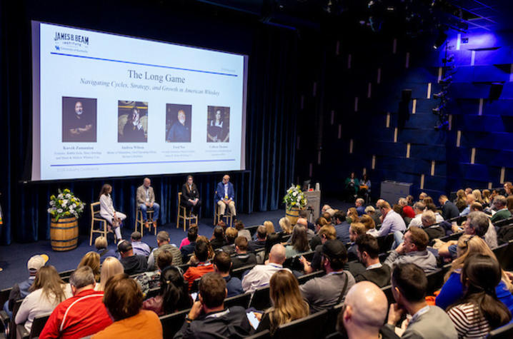photo of panelists discussion Four panelists beneath large screen presenting to an audience in a theater.