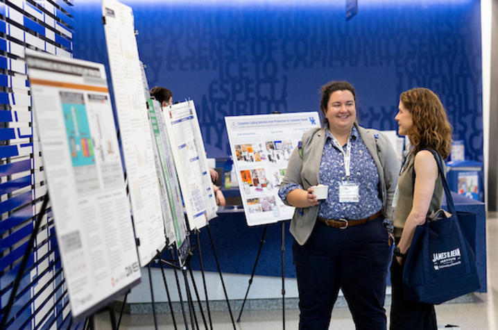 photo of research project displays Two people standing near research posters with a blue wall in the background.