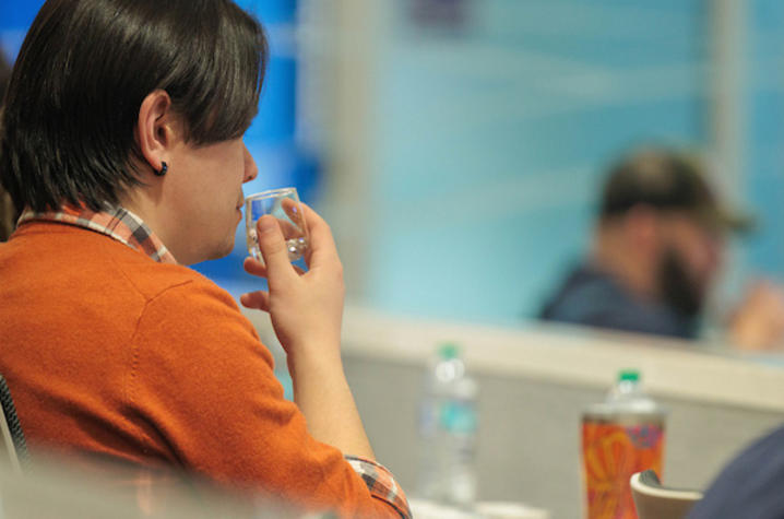 photo of bourbon tasting Photo taken from behind person wearing orange shirt and sniffing clear liquid in a small glass.