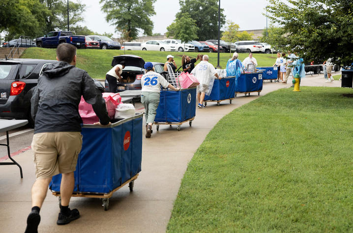 Volunteers push blue carts filled with students’ belongings along a wet campus sidewalk during UK’s Big Blue Move-In.