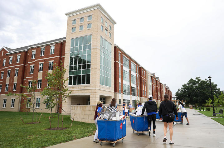 Students and volunteers push blue carts filled with belongings toward a UK residence hall during Big Blue Move-In.