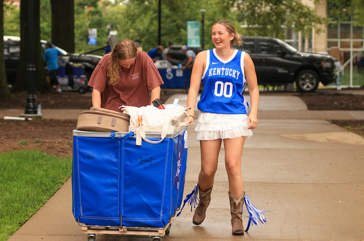 Two students laugh while pushing a blue cart filled with belongings during UK’s Big Blue Move-In.