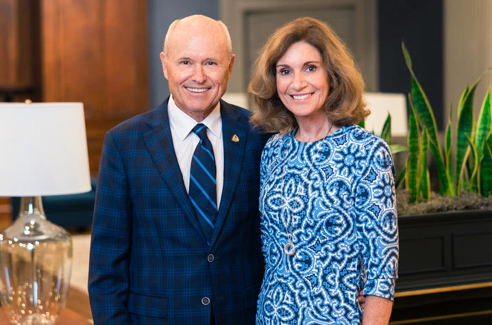Two people standing side by side indoors, posing for a portrait in front of decorative plants and lamps.