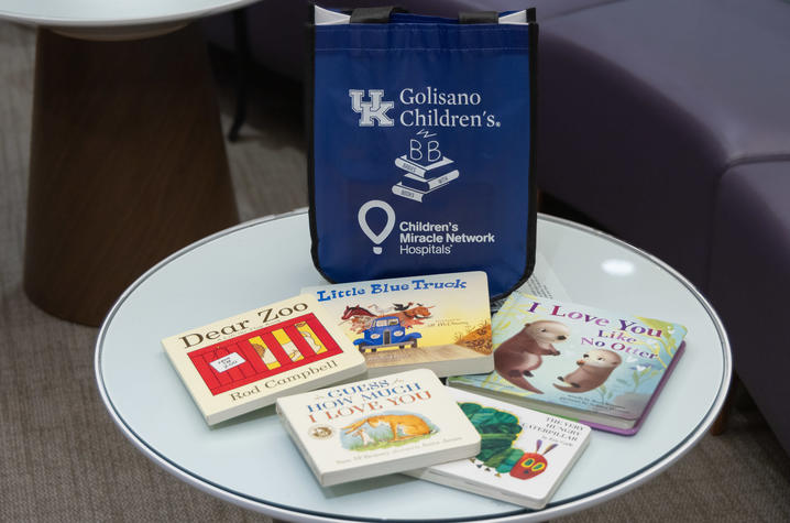 A blue Golisano Children’s Babies With Books tote bag sits on a round table surrounded by children’s board books, including Dear Zoo, Little Blue Truck, Guess How Much I Love You, I Love You Like No Otter and The Very Hungry Caterpillar.