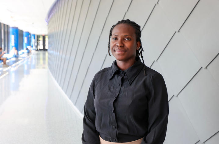 Portrait of a student standing in a bright campus hallway beside a modern gray wall.