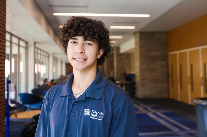 Person wearing a UK Financial Wellness polo stands in a campus building hallway.