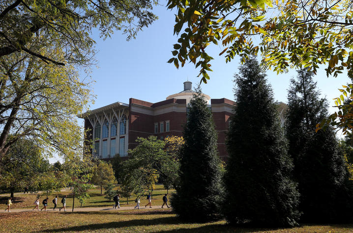 A brick campus building framed by trees and greenery on a sunny day.