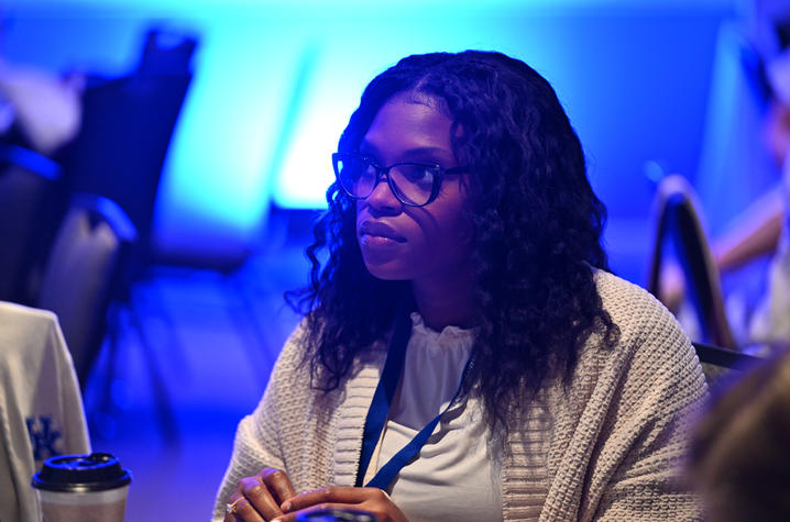 Sharonda Cox sits at a table and listens to a lecture during a sympsosium