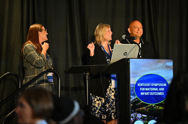 Three people stand on stage and present a lecture at a symposium