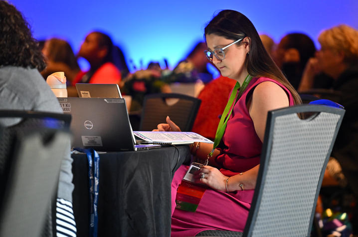 Cassandra Vargas sits at her laptop at a table during the symposium. she moderates a session online.