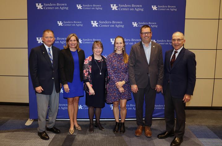Photo of speakers from the Sanders-Brown Center on Aging celebration Photo of men and women standing in front of blue backdrop.