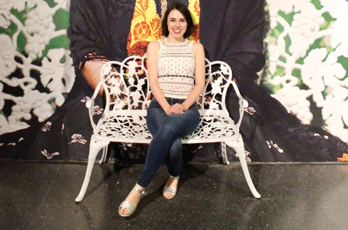 photo of Amaris Aleah Wade seated on white metal bench with mural of Frida Kahlo behind her
