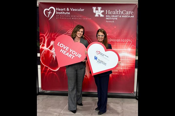 Two people stand smiling in front of a Heart & Vascular Institute and UK HealthCare Gill Heart & Vascular Institute Network backdrop, each holding a large heart-shaped sign, one reading “Love Your Heart.”