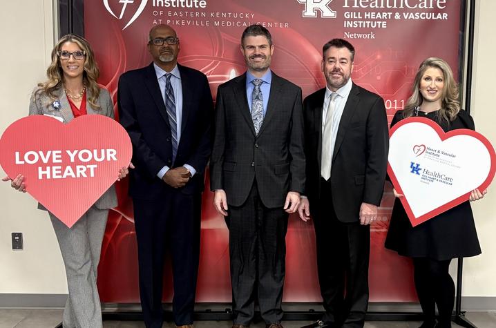 Five people stand in front of a Heart & Vascular Institute and UK HealthCare Gill Heart & Vascular Institute Network backdrop. Two are holding large heart-shaped signs, one reading “Love Your Heart.”