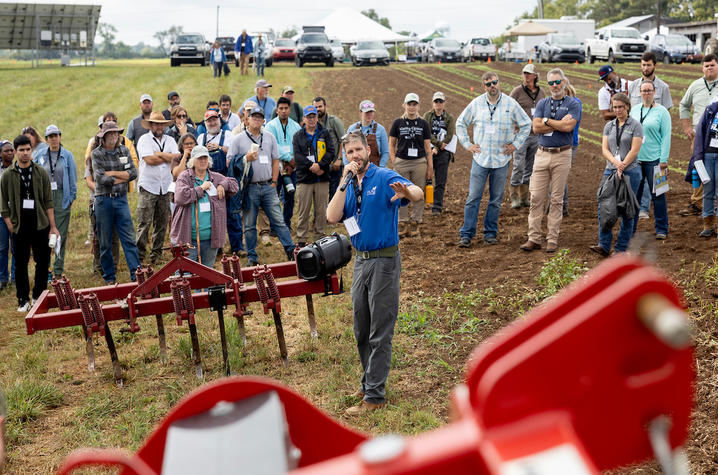 A large group of men and women standing listening to presentation at the 2025 Mechanical Weed Control Field Day