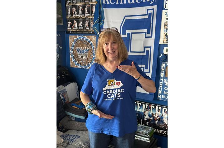 Person wears a blue T-shirt holds while standing in front of University of Kentucky-themed decorations.